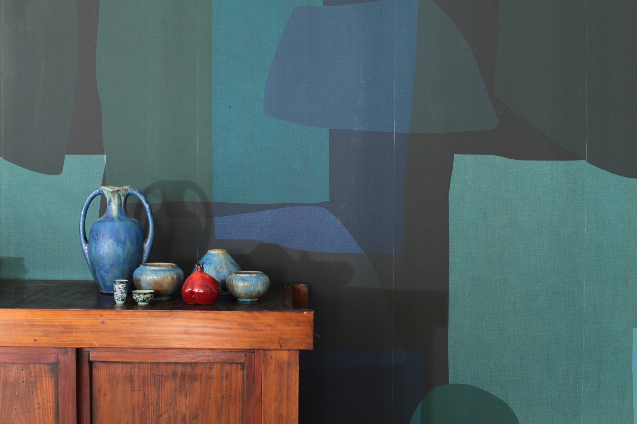 Blue vessels arranged on a wooden cabinet before an abstract teal and blue wall